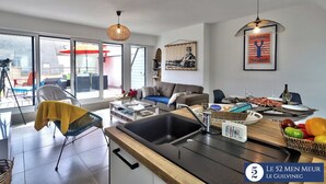 A modern living room with a kitchen area, large windows, and a dining setup. - 30 m2 terrace with sea view, 40 m from the beach and 300 m from shops (Guilvinec)