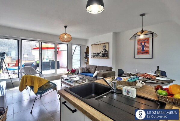 A modern living room with a kitchen area, large windows, and a dining setup.