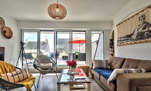Un salon moderne avec une table basse en verre, un canapé, un fauteuil et une grande fenêtre donnant sur la ville.