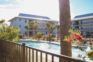A hotel with a swimming pool, palm trees, and a fenced deck area.