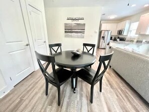 A dining area with a round table and four chairs, a kitchen in the background, and a sign that reads "Appalachian Sands".