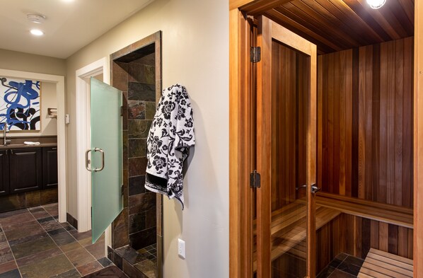 A modern bathroom with a glass shower door, a wooden sauna, and a patterned towel hanging on the wall.