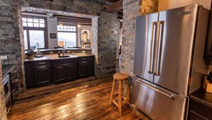 A kitchen with a stone wall, wooden floor, and a stainless steel refrigerator. - Ski-in/Ski-out, In the Village, 7 King Bedrooms, 2 Bedrooms w/ 2 XL twins (Sandpoint)