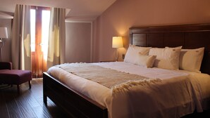 Ett hotellrum med en stor säng, en sänggavel i trä, en sänglampa och en stol.