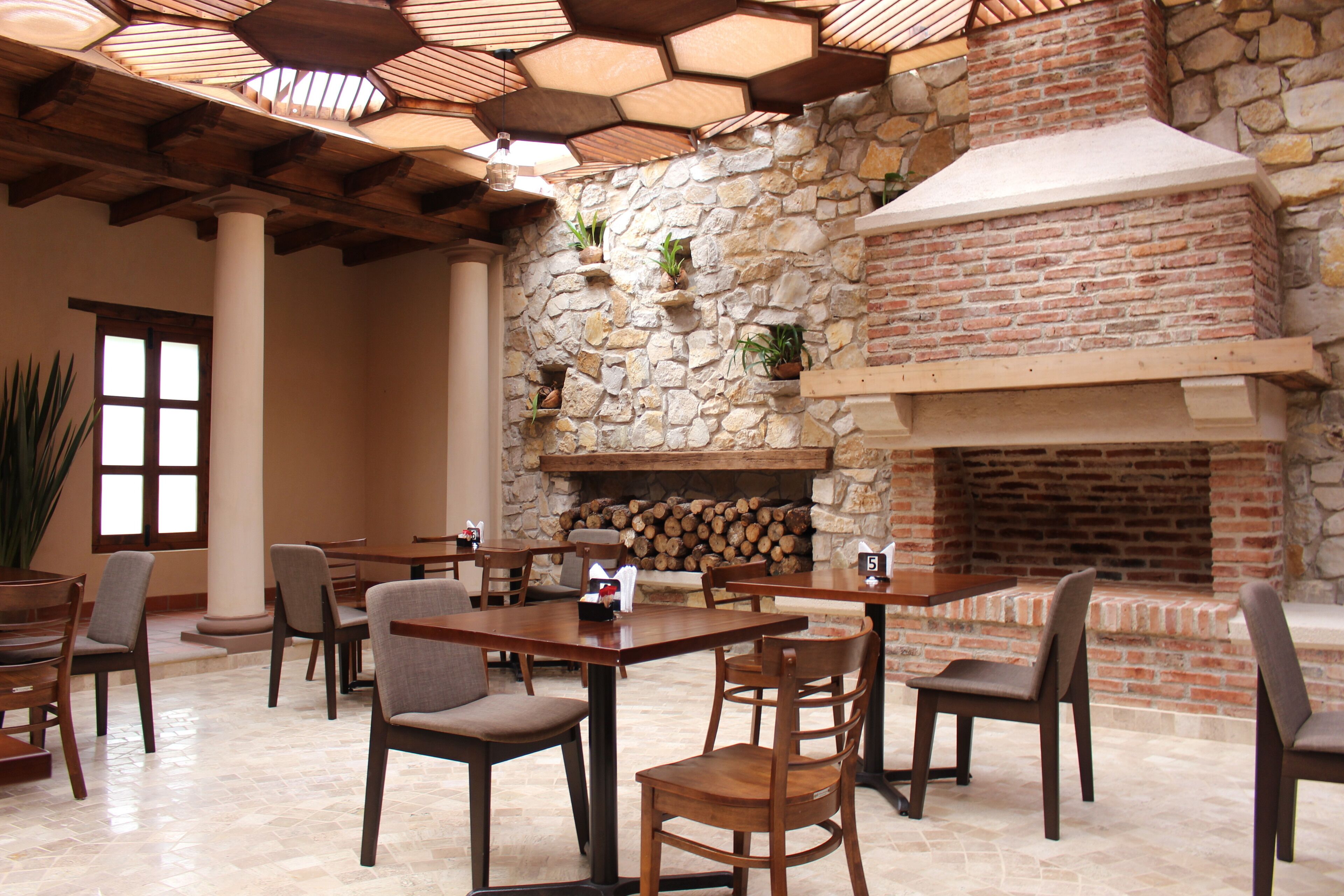 Un comedor con paredes de piedra, chimenea de ladrillo y varias mesas y sillas de madera.