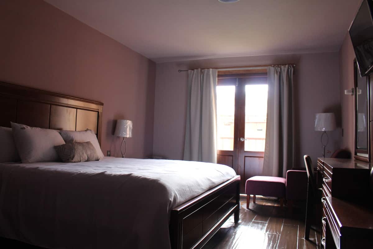 Une chambre d’hôtel avec un grand lit, un bureau, une chaise et une fenêtre avec des rideaux.