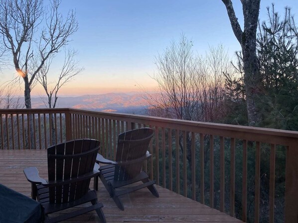 A wooden deck with two Adirondack chairs facing a mountainous landscape during sunset.