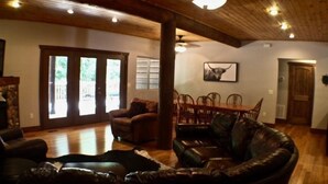 Un salón amplio con sofá de cuero, suelo de madera, zona de comedor con sillas y un ventanal con persianas.