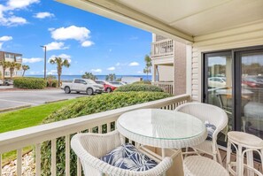A balcony with wicker furniture, a glass table, and a view of the beach and ocean. - 2BR Ocean Forest Villa Steps Away From Pristine Sandy Beaches 🏖️ Ocean View 🏖️ (Myrtle Beach)