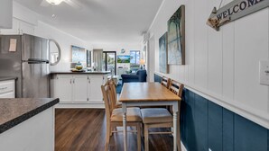 Una cocina moderna con armarios blancos, un refrigerador de acero inoxidable y un comedor con una mesa y sillas de madera.