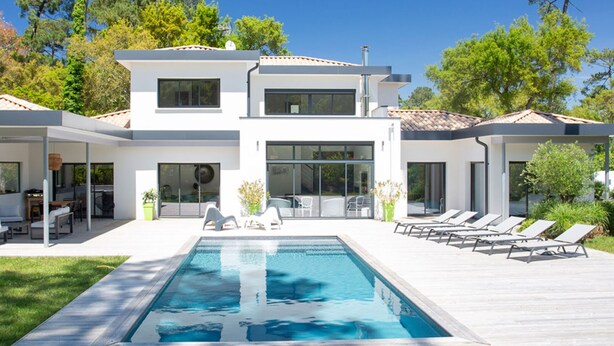 Une maison moderne à deux étages dotée d’une piscine, d’un espace salon extérieur et d’un patio couvert.