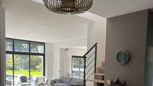 Un vaste espace de vie agrémenté d’un canapé gris, d’un escalier en bois et d’une grande fenêtre donnant sur l’extérieur.