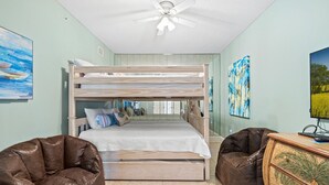 Camera con letto a castello, ventola a soffitto, due sacchi di fagioli e una cassettiera in legno.