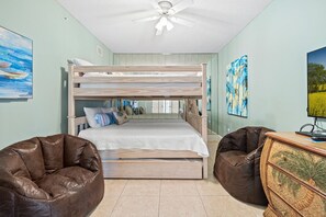 Ein Schlafraum mit Etagenbetten, Deckenventilator, zwei Sitzsäcken und einer Holzkommode.