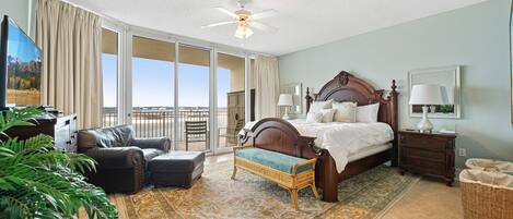 A spacious bedroom with a large bed, a sofa, a chair, and a balcony with a view.