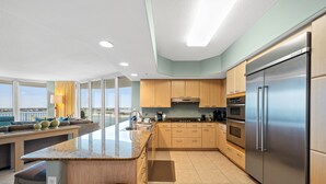 A modern kitchen with a large island, stainless steel appliances, and a view of the city. - Elegant Media Room Unit with Sparkling Bay Views! Complimentary Boat Slip! (Orange Beach)