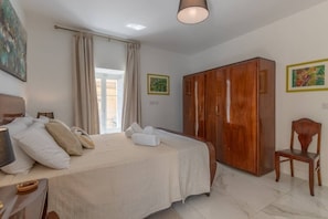 Un dormitorio con cama, un armario de madera, una silla y una ventana con cortinas.