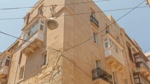 A multi-story building with a stone facade, balconies, and a staircase leading to the entrance.