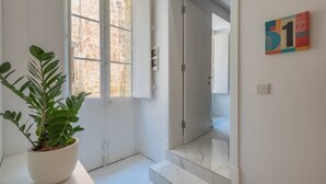 A clean, modern hallway with a potted plant, a glass door leading to another room, and a colorful artwork on the wall.