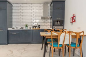 Una cocina con armarios oscuros, un salpicadero de azulejos blancos y un horno empotrado. Hay una mesa de comedor con sillas y un extintor de incendios colgado en la pared.