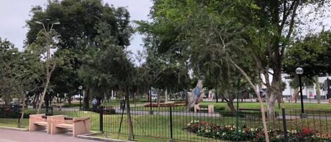 A park with a paved walkway, benches, and a fence with flowers.