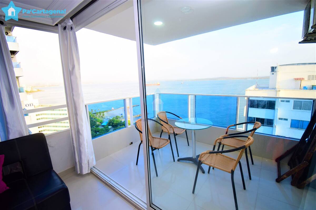 A balcony with a glass door, wicker chairs, a small table, and a view of the sea.