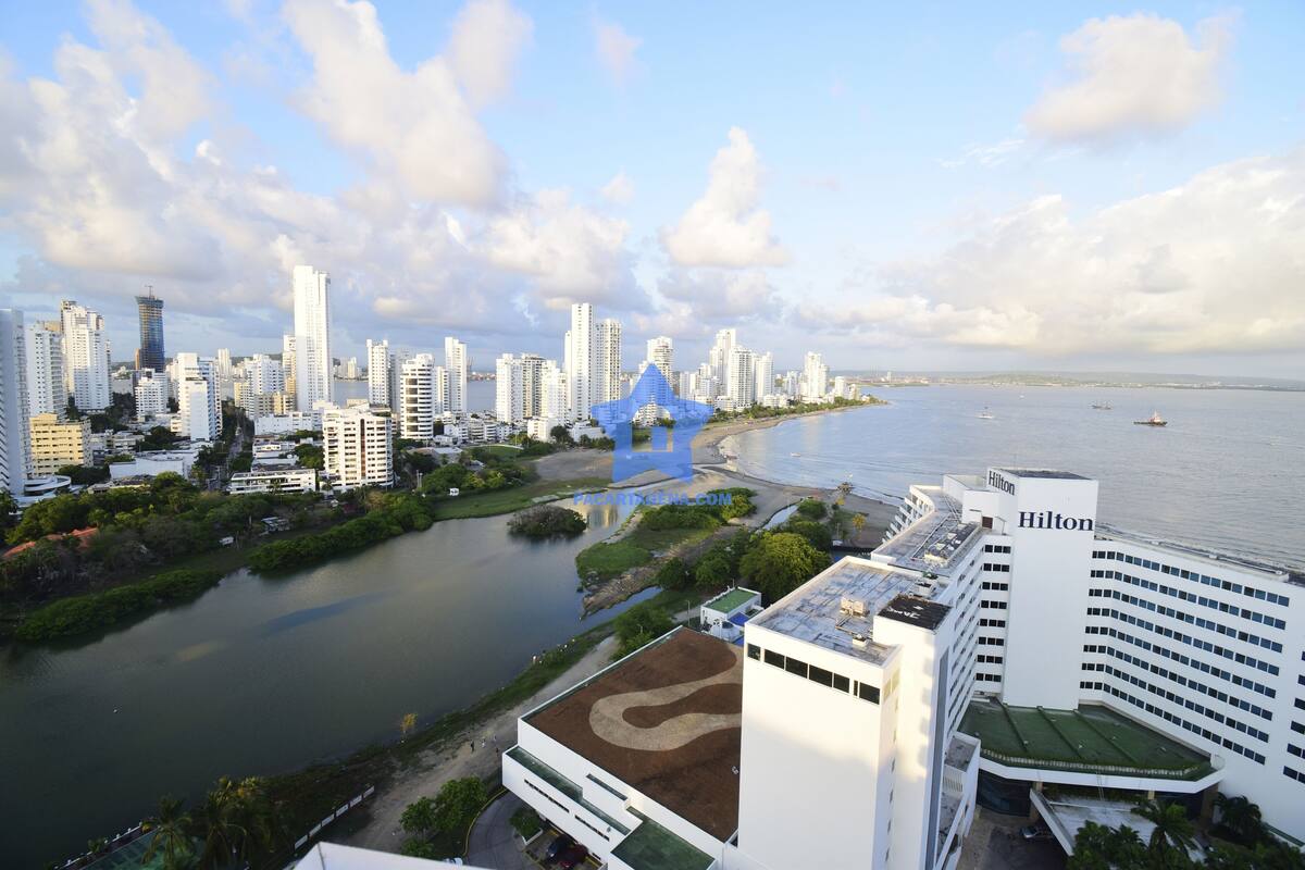 A high-rise hotel with a prominent Hilton sign, overlooking a river with a bridge and a cityscape in the background.