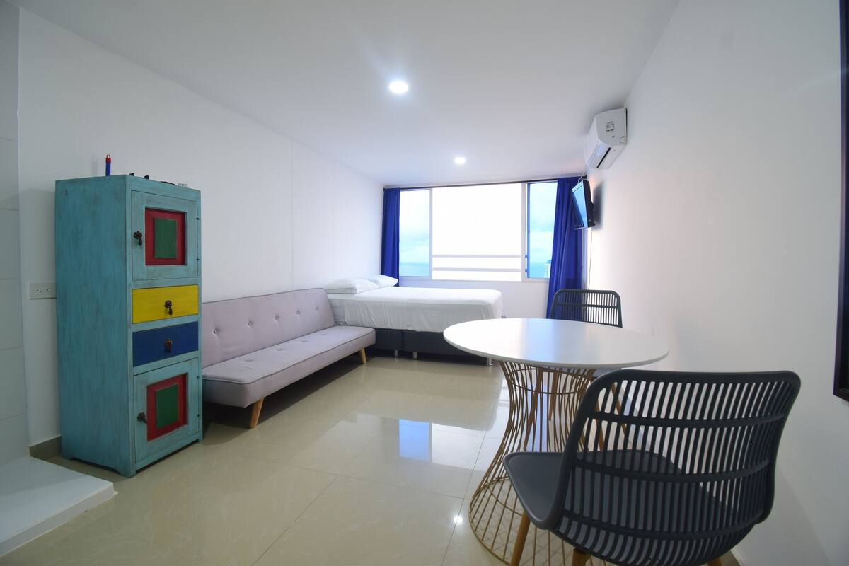 A modern room with a sofa, a dining table with chairs, a cabinet, and a large window with curtains.