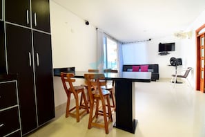 Une cuisine moderne avec des meubles de couleur noire, un îlot central doté de tabourets, un téléviseur à écran plat et un ventilateur de plafond.