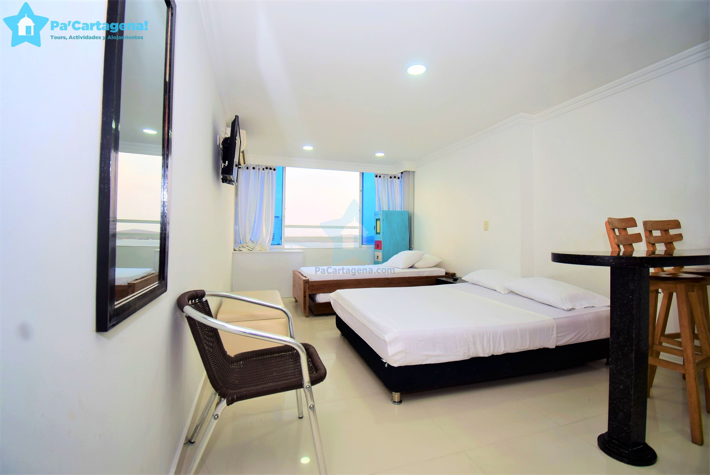 A hotel room with two beds, a chair, a table, and a TV.