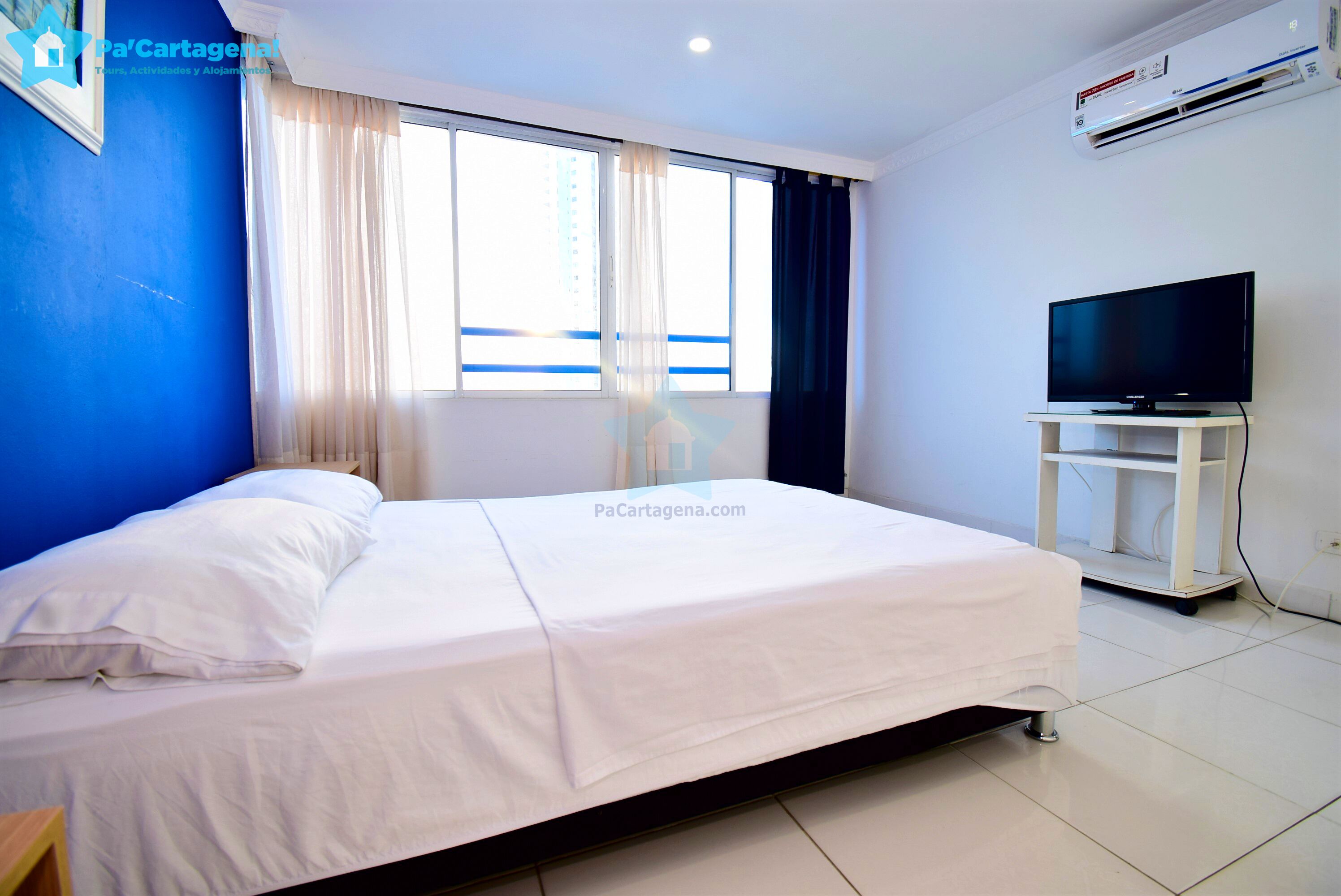 Une chambre d’hôtel avec un lit, un téléviseur posé sur un meuble et un appareil de climatisation fixé au mur.