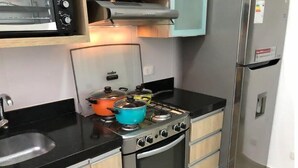 Une cuisine compacte équipée d’une cuisinière à gaz, d’un four et d’un micro-ondes encastré. On y trouve des armoires en bois et un réfrigérateur en acier inoxydable.