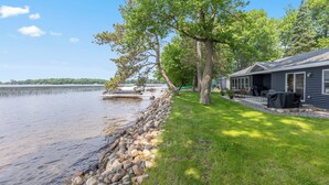 A lakeside property with a dock, a covered outdoor seating area, and a stone retaining wall. - Lakefront on Platte Lake - 5BR/4BA - Sleeps 18 - 2 King Suites - Pontoon Rental (Hillman)