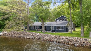 Un chalet au bord du lac doté d’une grande terrasse, d’un espace salon extérieur couvert et d’un mur de soutènement en pierre.