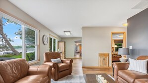Un salon spacieux, doté de canapés en cuir, d’une table basse en bois et offrant une vue sur un lac grâce à de grandes fenêtres.
