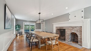 Un comedor amplio con una larga mesa de madera y sillas, una chimenea y vistas al exterior.