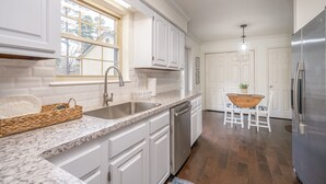 A kitchen with white cabinets, a granite countertop, stainless steel appliances, and a dining area with a wooden table and chairs.