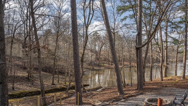 A wooden deck with chairs and a fire pit, surrounded by trees and a lake.