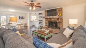 A living room with a stone fireplace, a ceiling fan, and a dining area in the background.