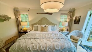 A neatly made bed with a headboard, two bedside lamps, and a window with curtains.