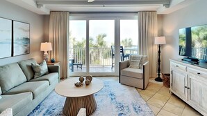 Ein modernes Wohnzimmer mit Sofa, Sesseln, Couchtisch, Fernseher und Balkon mit Gartenmöbeln.