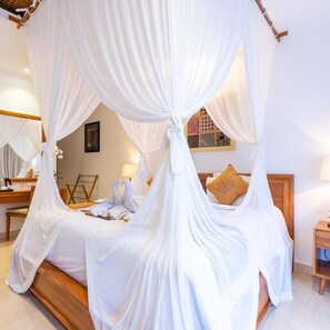 A room with a four-poster canopy bed, a wooden headboard, a bedside table with a lamp, and a wall-mounted mirror. - Villa Sonia Bisma (Ubud)