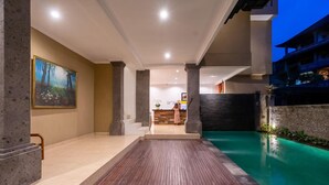 Un moderno vestíbulo de hotel con mostrador de recepción, una terraza de madera y una zona de piscina.