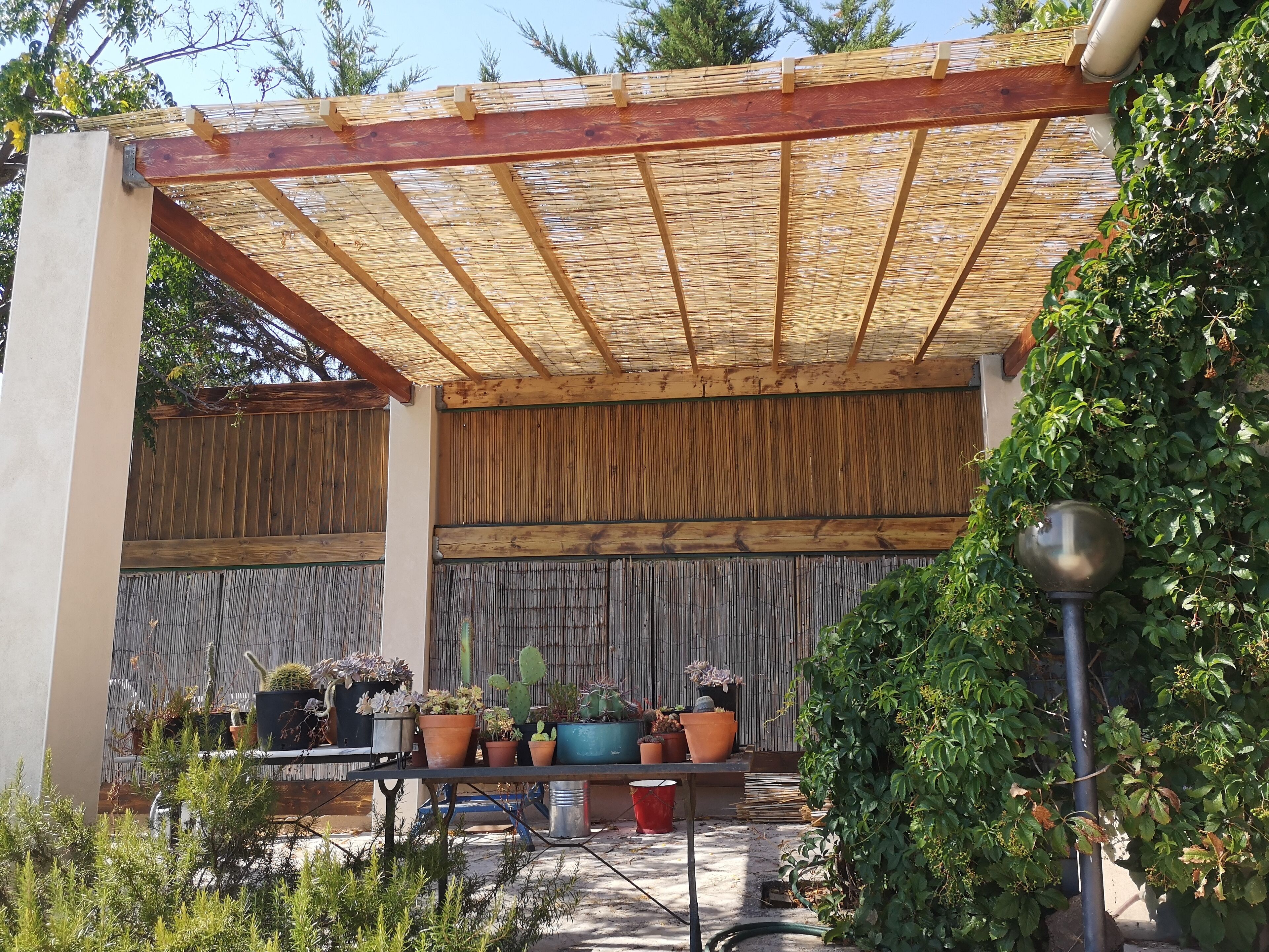 Un patio abrité doté d’un toit en bambou, de poutres en bois et de diverses plantes en pot.