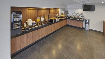 A buffet setup with a coffee machine, juice dispensers, and various food items.
