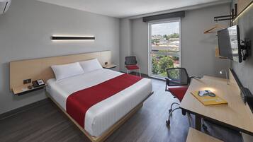 A hotel room with a large bed, a desk with a chair, a TV, and a window with a view of buildings.