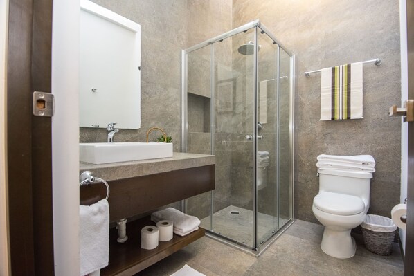 A modern bathroom with a glass-enclosed shower, a white sink, and a toilet.