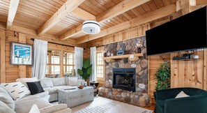 A cozy cabin interior with a stone fireplace, wooden beams, a sofa, and a television. - Wander Inn - Updated Log Cabin near shared beach (Saugatuck)