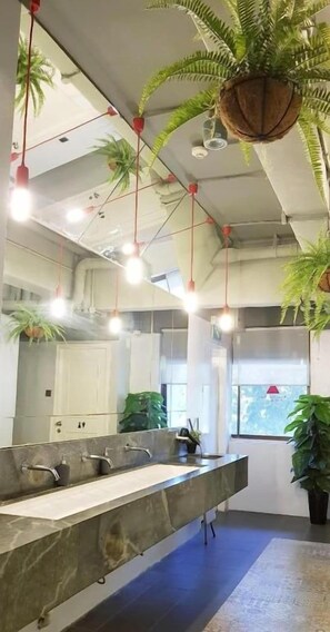 A modern bathroom with a long sink, multiple hanging lights, and several potted plants.