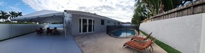 outdoor space with a swimming pool, seating area, and tent, surrounded by a fence and palm trees.